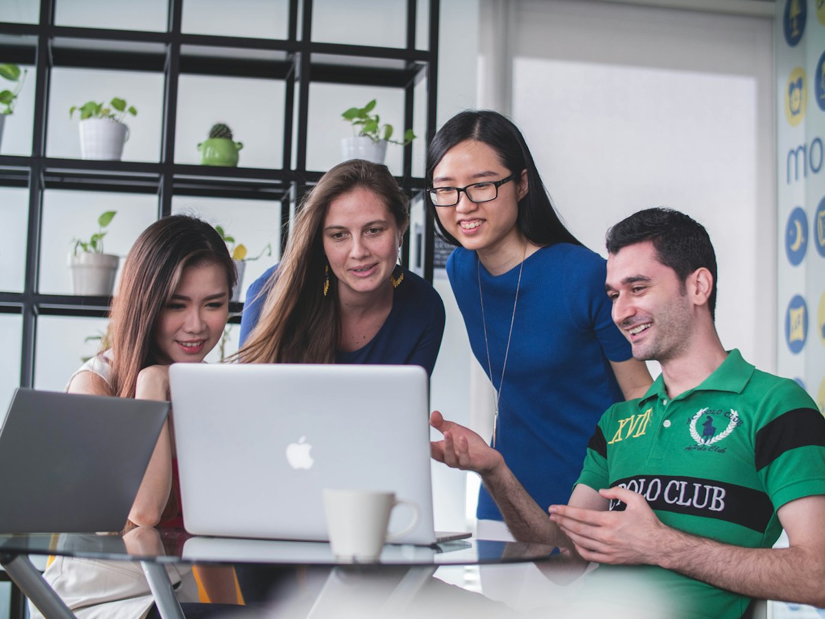A team gathered around a laptop, smiling as they work through something together