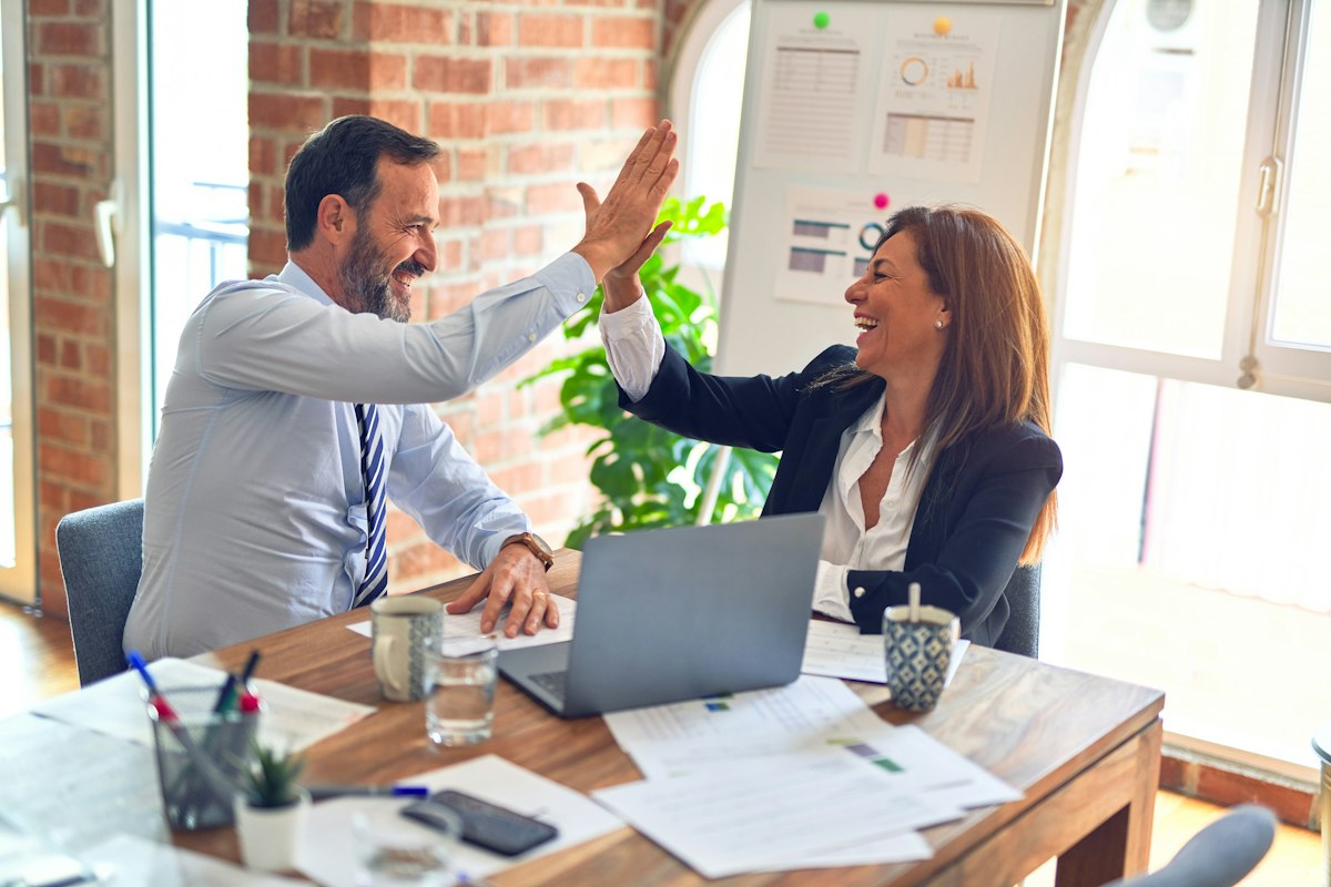 Two colleagues high-fiving across a desk after getting something done